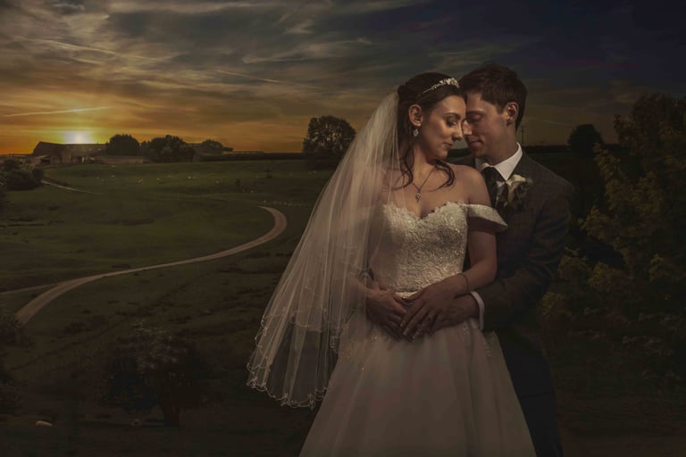 Newlywed couple posing for a romantic wedding portrait in front of a rural sunset landscape.