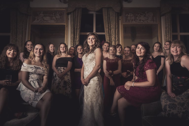 Smiling bride in white lace gown poses with her bridesmaids in formal dresses at a wedding reception.