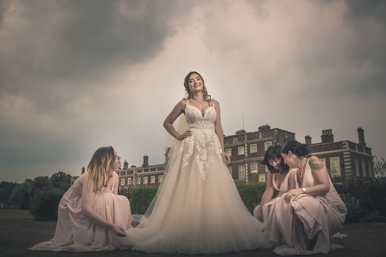 Smiling bride in a lace wedding dress with bridesmaids in pink gowns at a historic estate.