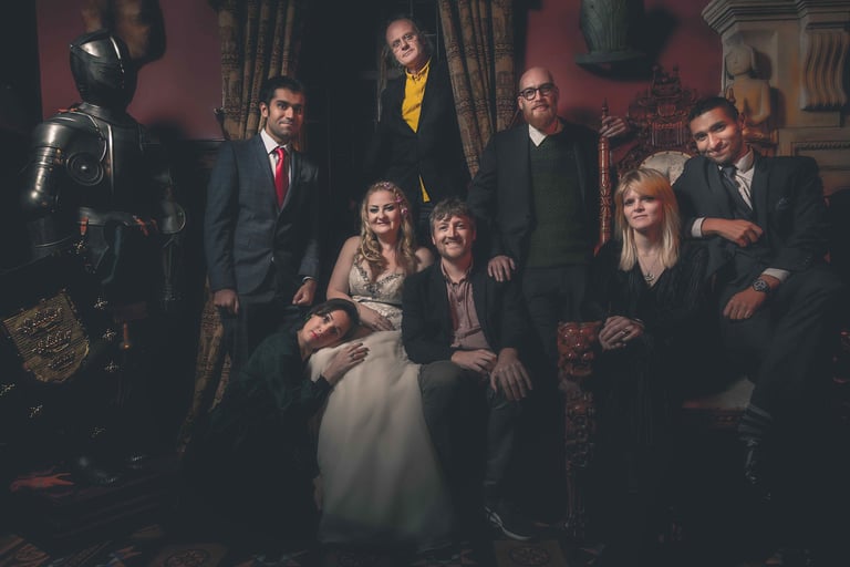 A diverse group in formal attire posing in a gothic room with a medieval knight suit of armor.