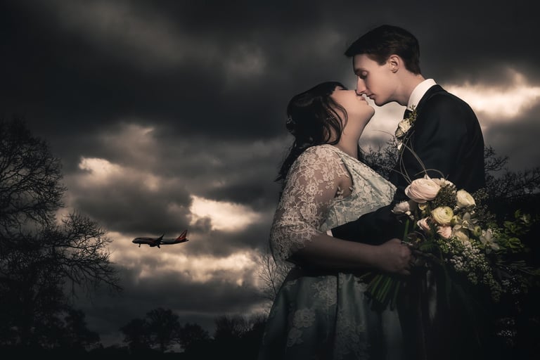 A bride and groom sharing a romantic kiss under dark storm clouds with a plane flying in the background.