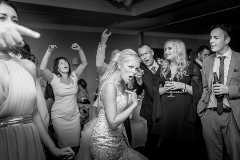 A joyful bride dancing with wedding guests during a black and white reception celebration.