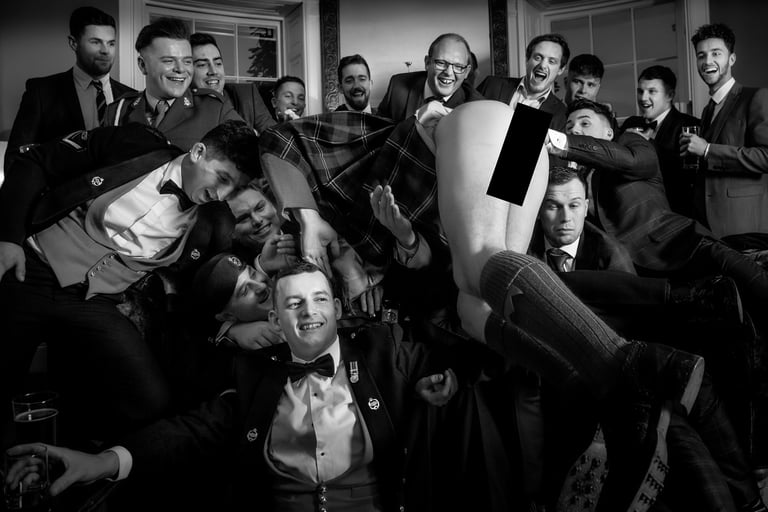 A group of men in formal suits and kilts celebrate in a black and white group photo.
