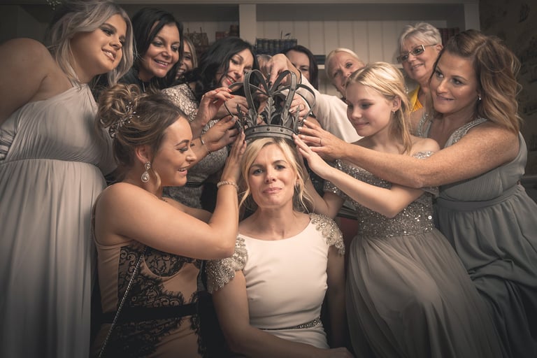 A group of bridesmaids and family placing a vintage metal crown on a bride's head at a wedding.
