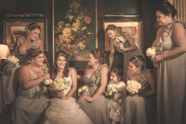 Smiling bride and bridesmaids in elegant sage dresses holding cream rose bouquets for a wedding portrait.