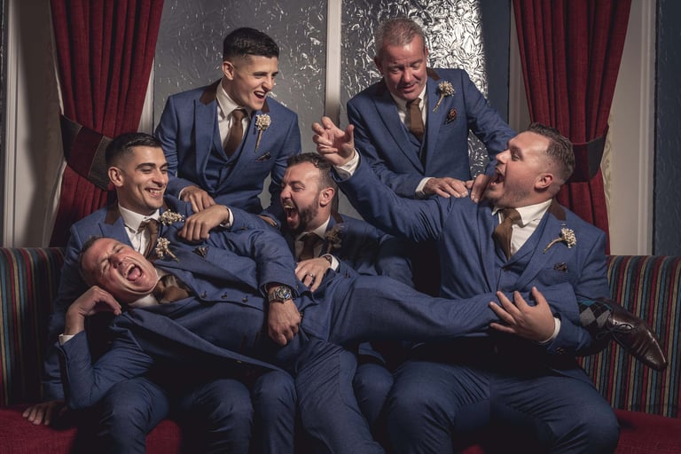 Groom and groomsmen in blue three-piece suits laughing together during a wedding celebration.