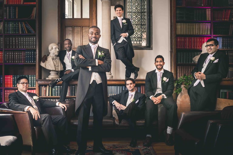 Groom and groomsmen in formal morning suits posing in a classic library for a wedding photo.