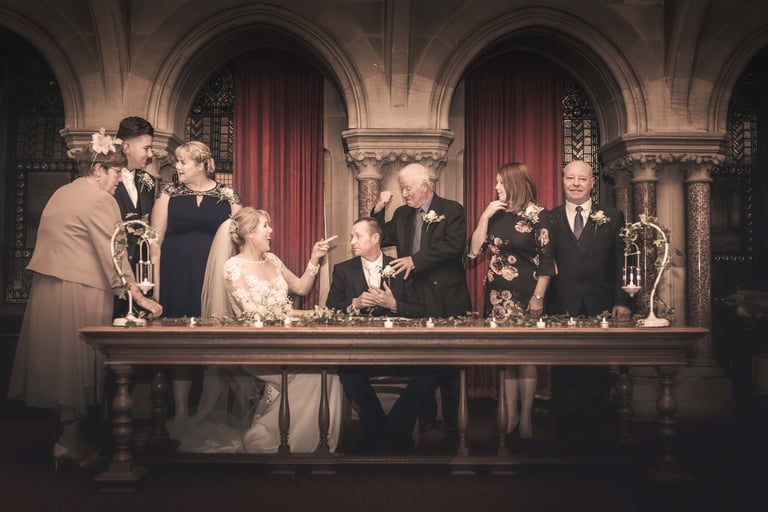 A joyful wedding couple and family posing at a vintage registry office signing table.