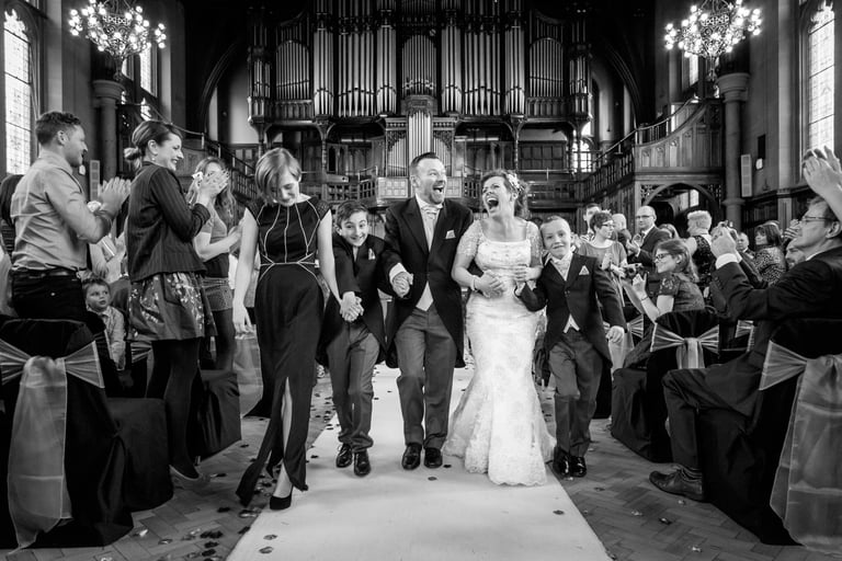 Black and white photo of a happy bride and groom walking down the aisle after a church wedding ceremony.