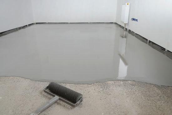 Freshly poured self-leveling floor compound with a spiked roller for smoothing gray epoxy.