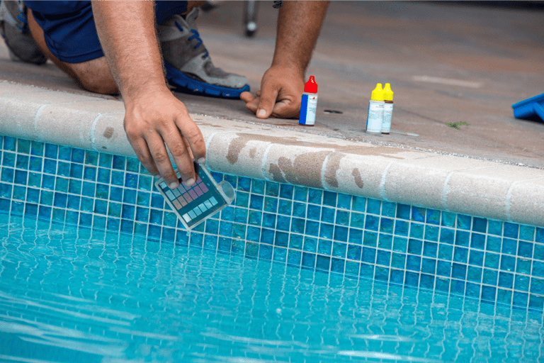 Close-up image of a pool tech kneeling on the edge of a pool performing water testing and balancing