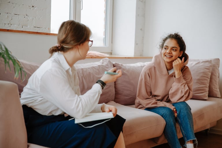 An adolescent girl sitting on a couch smiling and talking to a female therapist