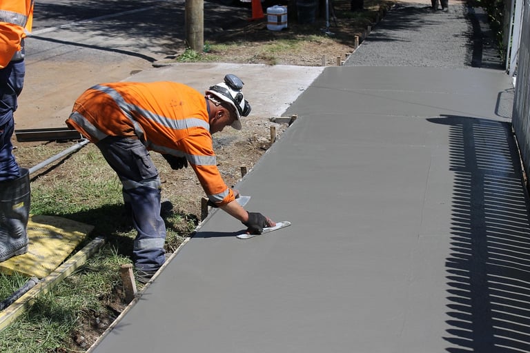 a man in a helmet and safety vest is  working on a wet concrete