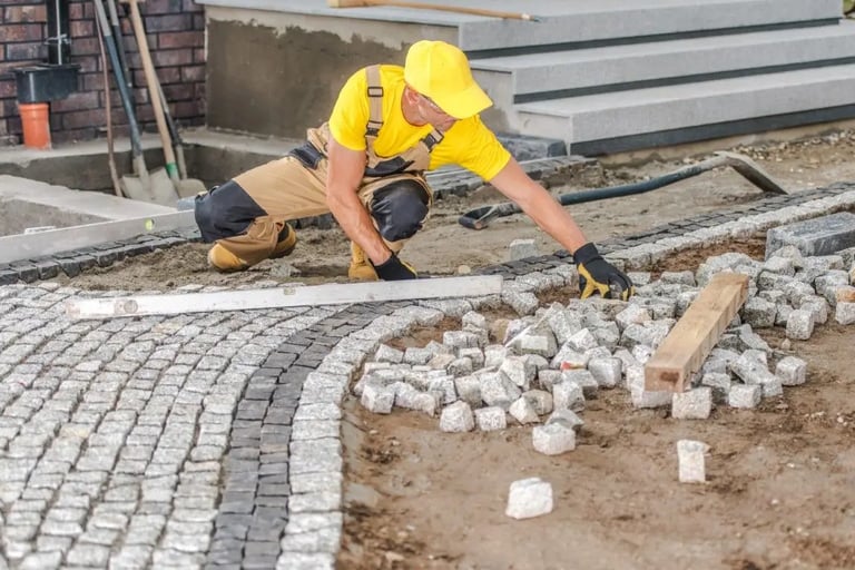 a man in a yellow shirt is laying concrete bricks on the ground