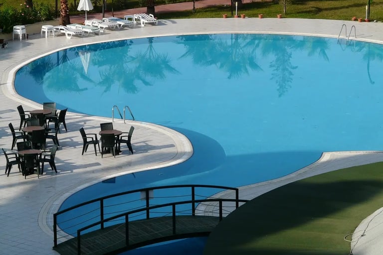 a pool with concrete deck, chairs and tables in a resort