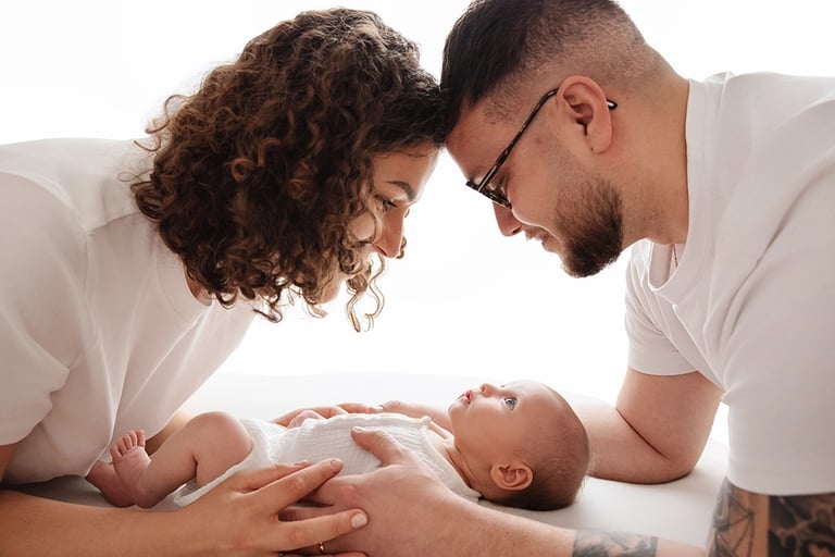 photo de bébé avec ses parents au dessus de lui et les regarde