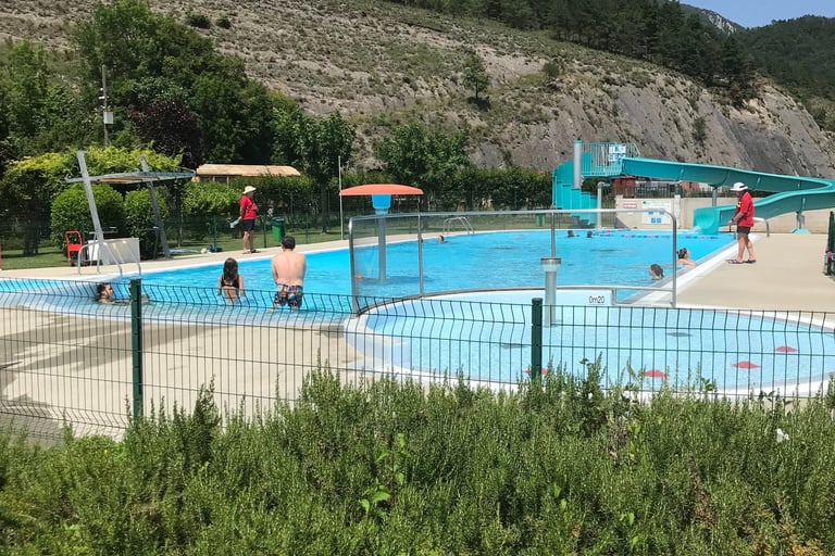 Families enjoy an outdoor swimming pool with water slides at a mountain resort in Axat