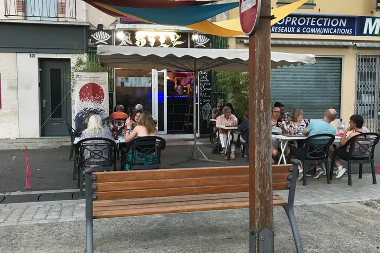 Customers dining at a cozy outdoor restaurant terrace with colorful sun sails. Asily Quillan.