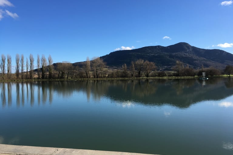 Serene landscape featuring a calm lake reflecting tall trees and a dark mountain  in Puivert.