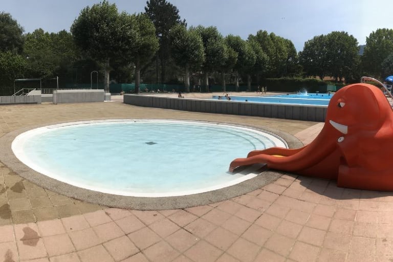 Round outdoor kiddie pool with a red elephant slide at a sunny public swimming Qiullan.