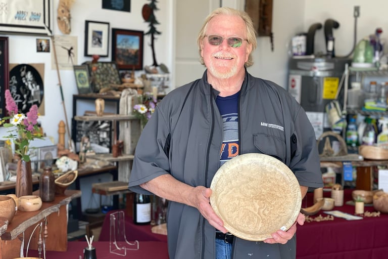 Woodturner Tom Baker holding his Big Leaf Maple Burl Platter, in front of show display