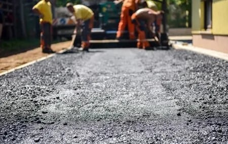 Men spreading ashpalt ahead od the asphalt paver. 