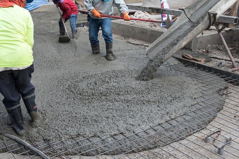 workers spreading concrete that is coming off concrete truck