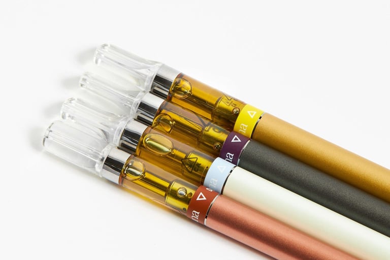 Four cannabis vape cartridges with golden distillate oil attached to colorful slim battery pens.
