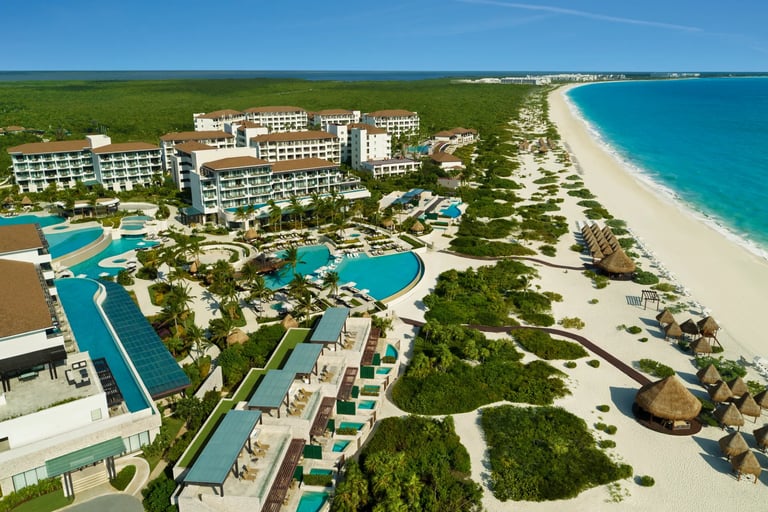 Aerial view of a luxury beachfront resort in Cancun with swimming pools, white sand, and turquoise ocean water.
