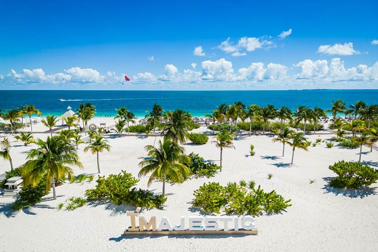 Aerial view of Majestic Resorts white sand beach with palm trees and turquoise Caribbean water.