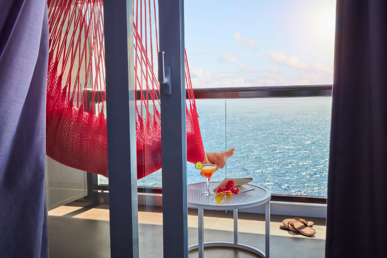 Relaxing on a luxury cruise ship balcony in a red hammock with ocean views and a tropical cocktail.
