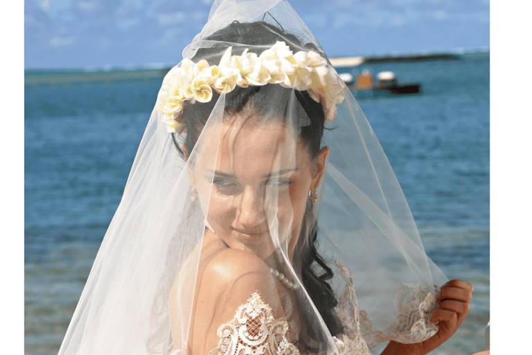A bride with a flower crown and white lace veil during a tropical beach wedding ceremony.