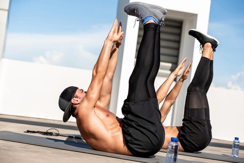 Two people performing toe touch abdominal crunches outdoors on yoga mats for core strength.