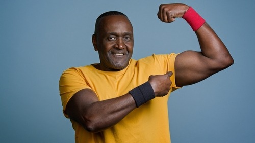 Fit senior Black man in a yellow t-shirt flexing bicep muscles showing strength and health.