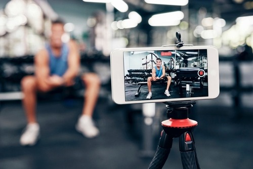 Fitness influencer filming a workout video at the gym using a smartphone on a tripod.