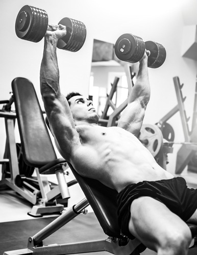 Muscular man performing an incline dumbbell chest press during a bodybuilding gym workout.