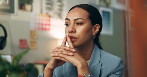 A pensive female professional in a blue blazer brainstorming at her creative office desk.