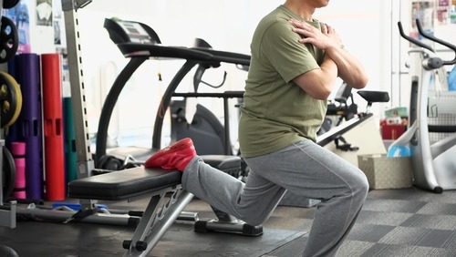 A man performing a Bulgarian split squat using a gym bench for leg strength training.