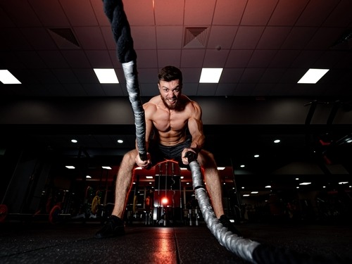Muscular man doing high-intensity battle rope workout for core strength in a dark gym setting.
