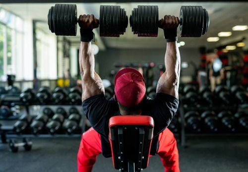 Muscular bodybuilder performing a heavy dumbbell bench press for chest strength training in a gym.