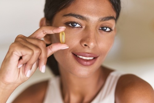 Smiling woman holding a yellow omega-3 fish oil softgel capsule for daily health and wellness.