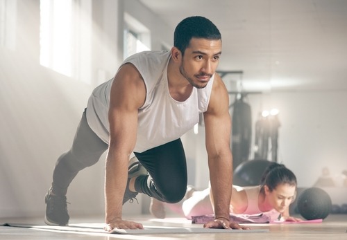 A fit man performing mountain climber exercises on a mat during a gym workout session.