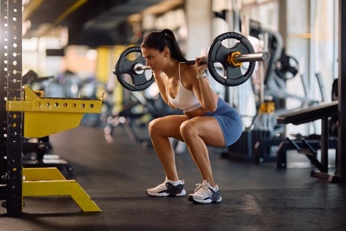 Athletic woman performing a barbell squat for strength training in a modern gym.