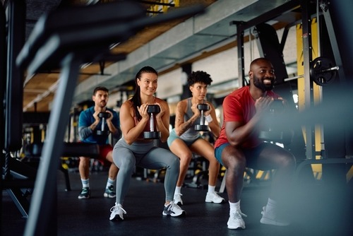 Diverse group of athletes performing goblet squats with dumbbells during a fitness class in a modern gym.