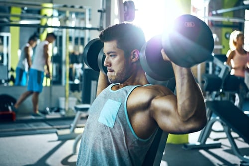 A muscular man performing a seated dumbbell shoulder press in a modern gym for strength training.