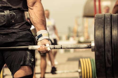 A muscular weightlifter with chalked hands lifting a heavy barbell during a powerlifting competition.