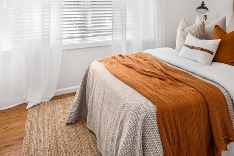 bright bedroom with honey or rust colored throw and pillow with linen rug, fall color