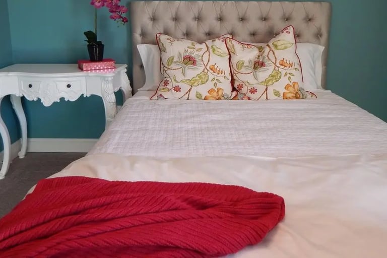 bedroom with teal walls with fall decor accents of a burgundy throw and two fall decorated pills