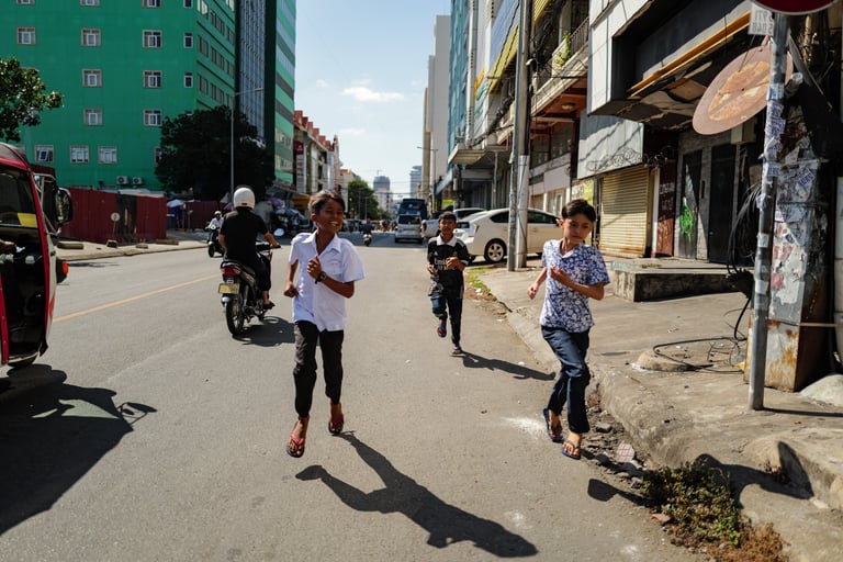Childrens running down a street during a sunny day in Phnom Penh, Cambodia - by ACAT PHOTOS
