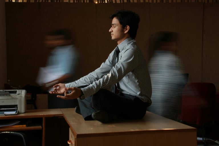 Man meditating on his desk in a busy office